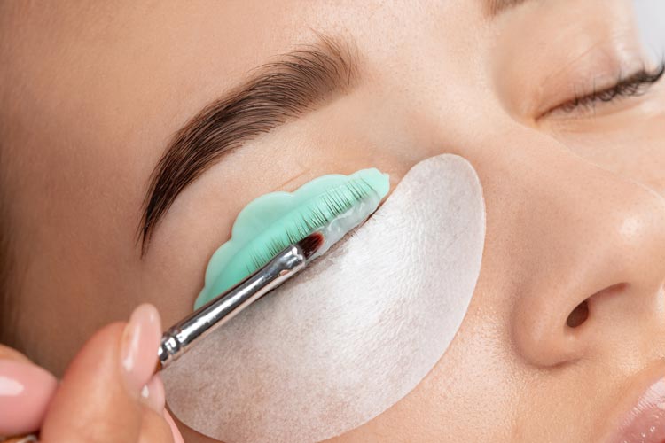 Fransstylist applicerar lashliftmedel på en kvinnas ögonfransar med skyddsplåster under ögat