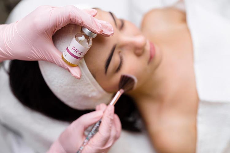Hudterapeut applicerar PRX-T33 kemisk peeling med pensel på kvinna som ligger avslappnad